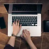 Top view of hands typing on a laptop with a camera positioned to the side.